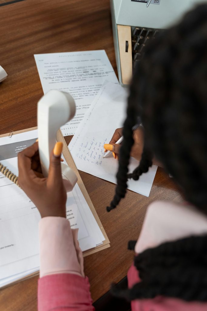 A lady holding a phone and writing something on a paper