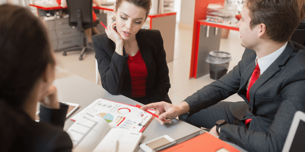 A man and woman in business attire engage in conversation, standing close together in a professional setting.